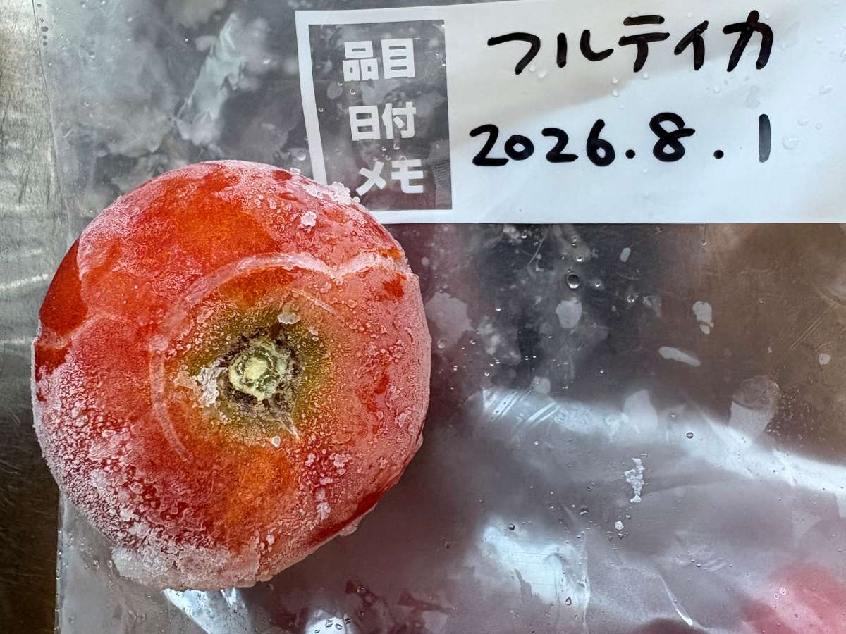 保存袋に入れて冷凍した中玉トマト「フルティカ」。表面に霜がつき、ヘタを取った跡が見える。袋のラベルには品目「フルティカ」と日付「2026.8.1」を記入。庄内の家庭菜園で採れた裂果の実